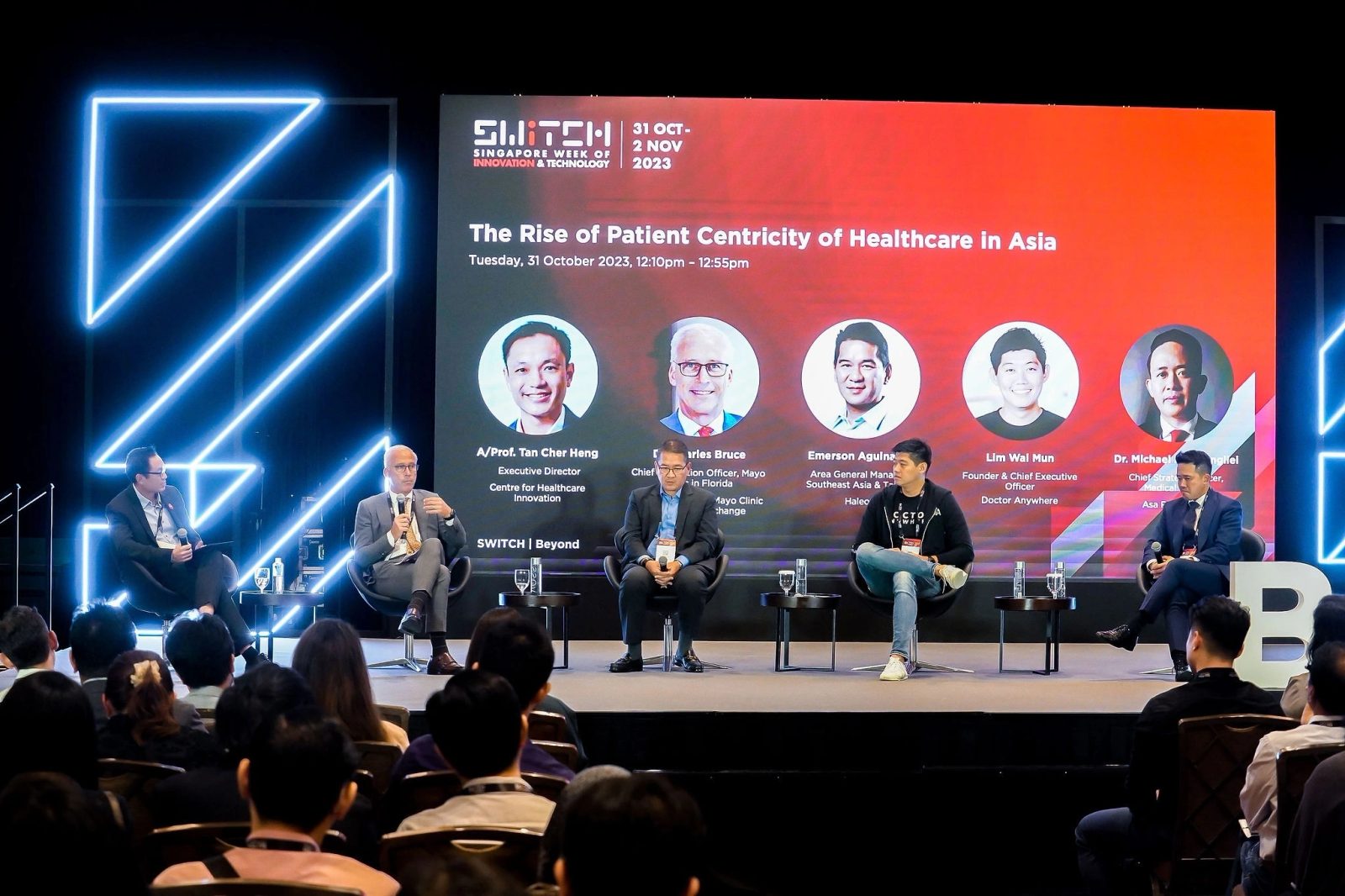 Healthcare panel on a conference stage with a full LED backdrop and seated audience