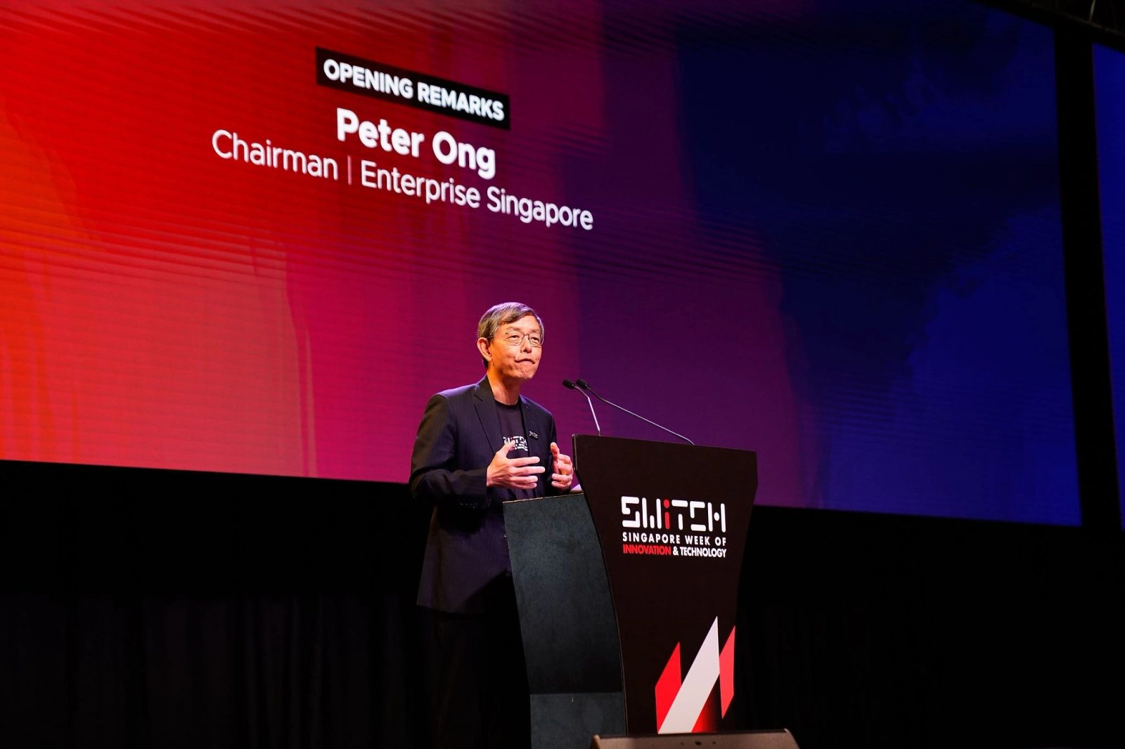 Keynote speaker delivering opening remarks at a podium under stage lighting